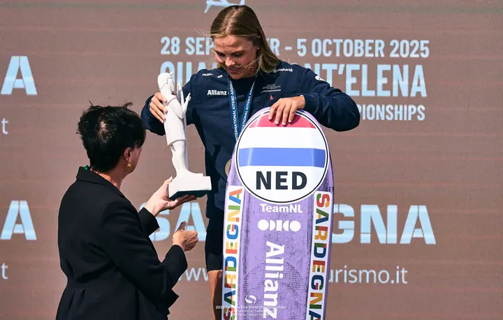 Jessie Kampman taking the world championship trophy, her board beside her showing the Dutch flag, the event backdrop behind her reading 28 September to 5 October 2025.